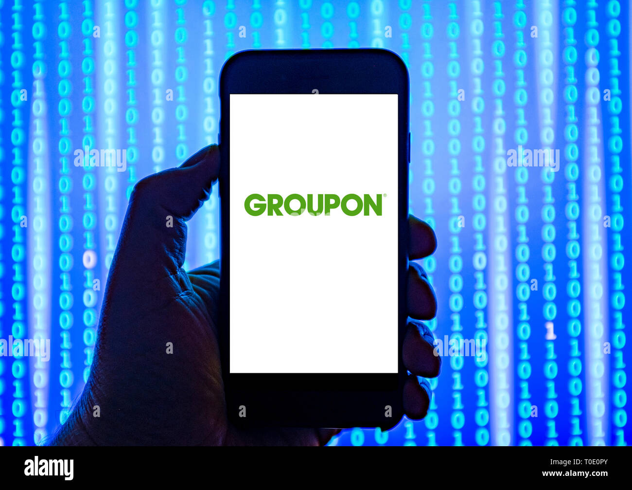 Person holding smart phone with Groupon logo displayed on the screen. Stock Photo
