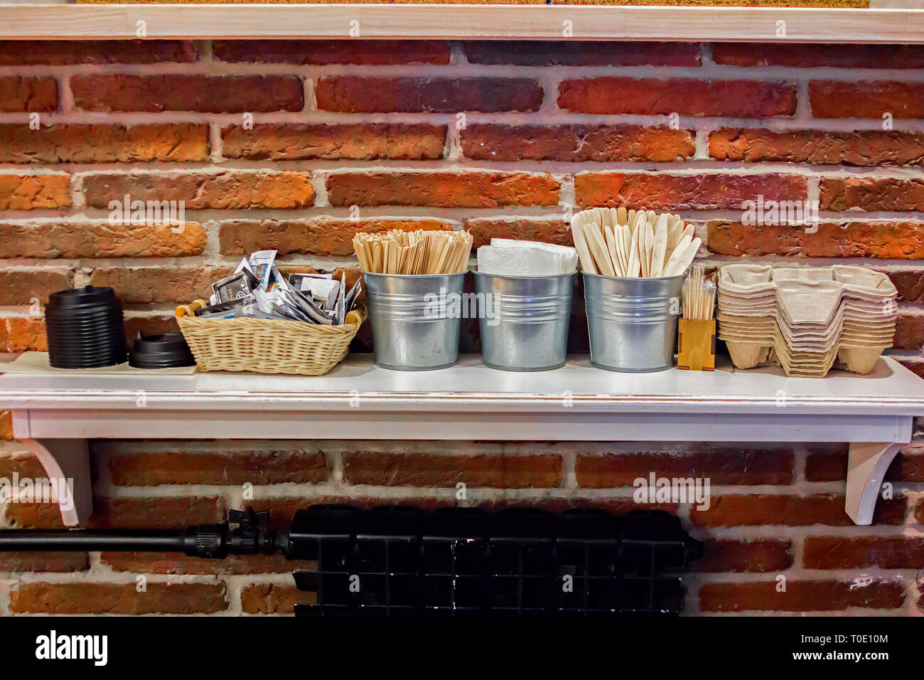 Close-up view of various disposable wooden sticks, wooden spoon, tooth sticks, cup covers, Take away boxes, napkins and sugar bags on wooden counter Stock Photo