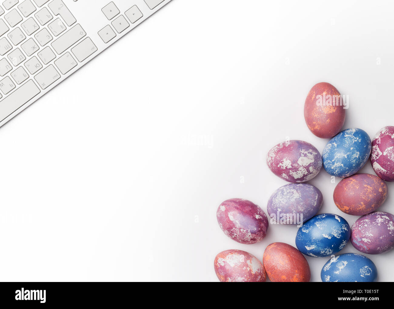 Easter multicolored eggs in right corner with keyboard in left corner isolated on white background. Concept of Easter card, free space for text. Flat  Stock Photo
