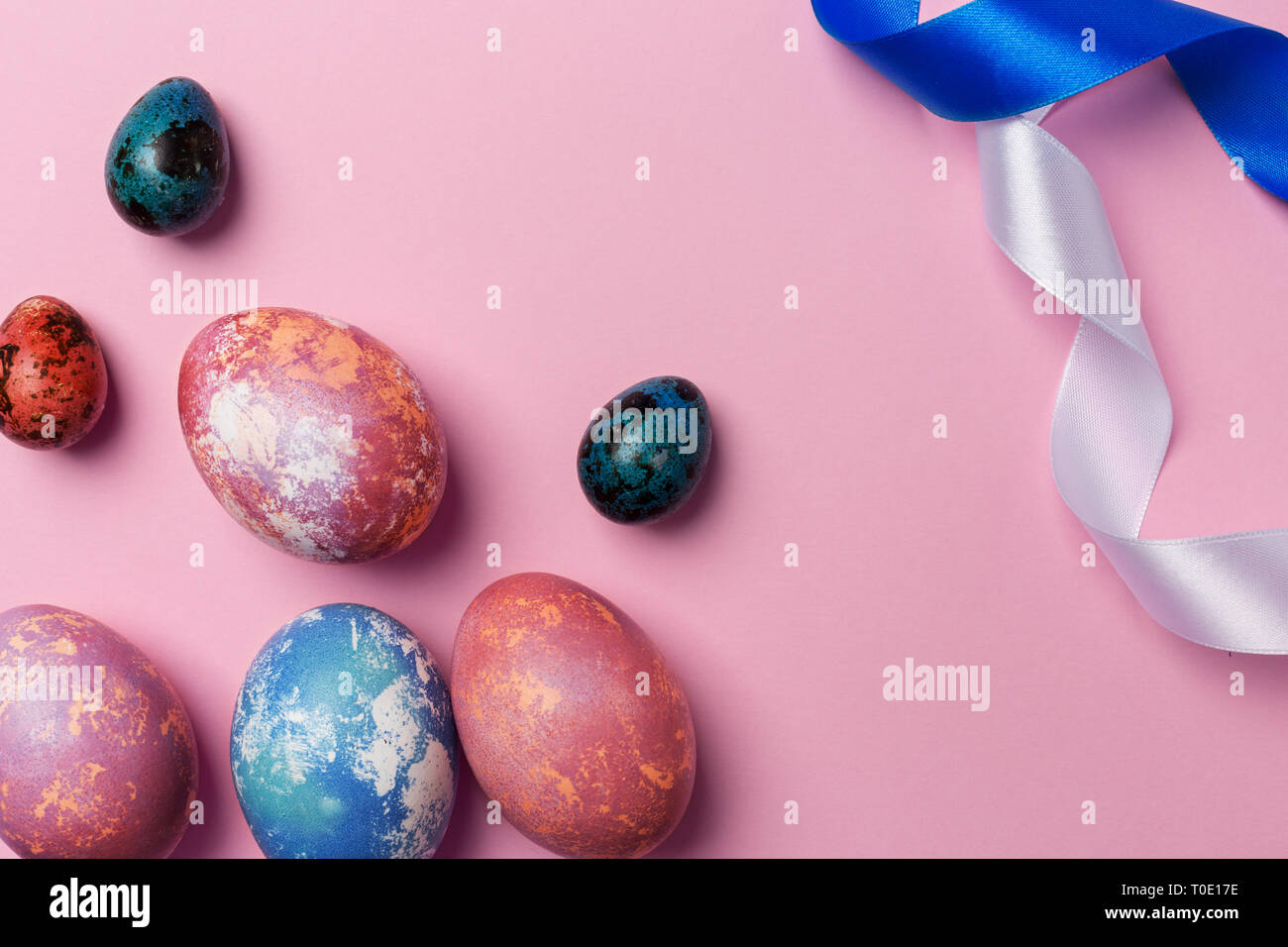 Close up Easter colorful eggs with white and blue ribbon on pink background. Space for text, concept of Easter background Stock Photo