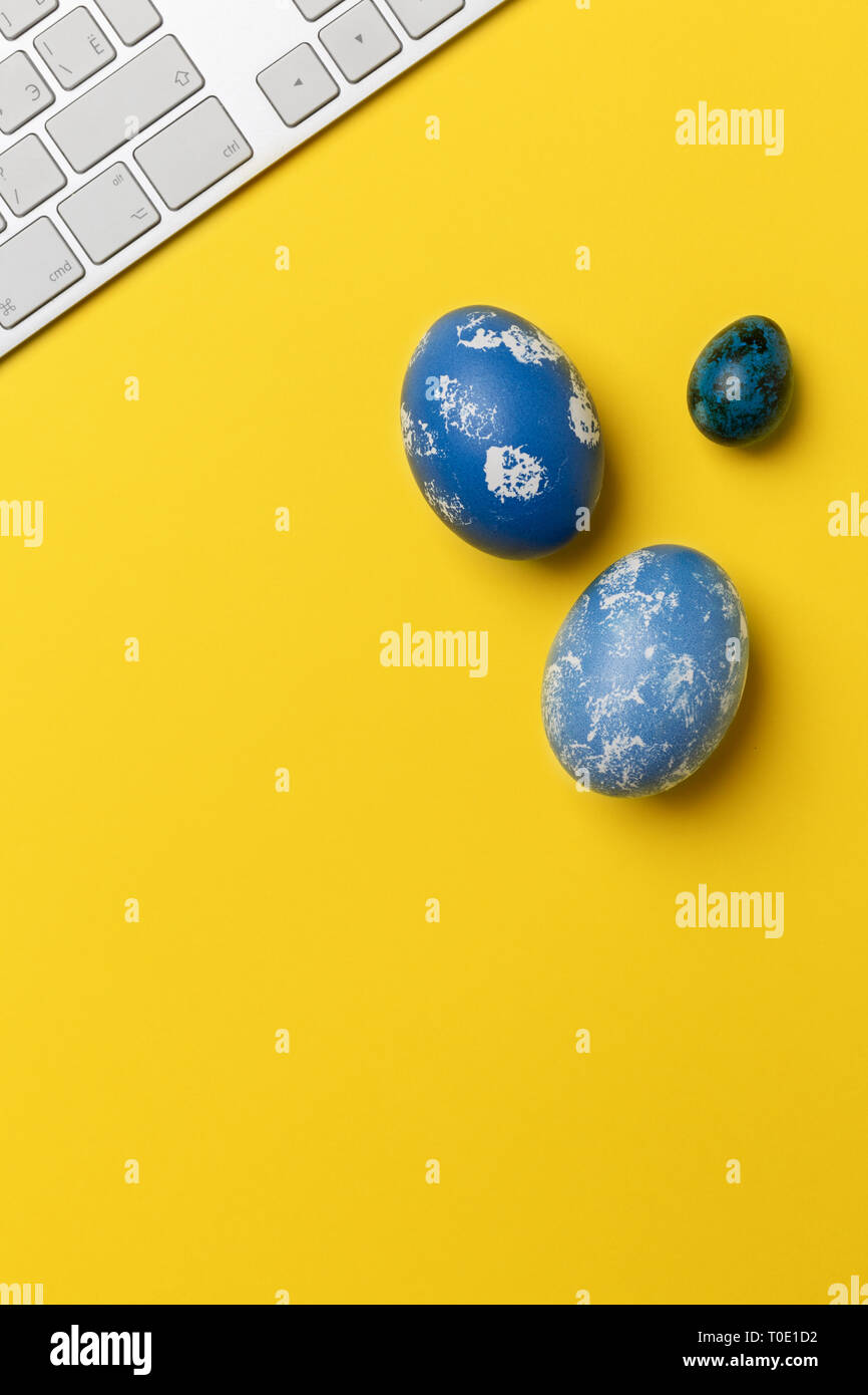 Blue Easter eggs with keyboard on yellow background. Concept of office
