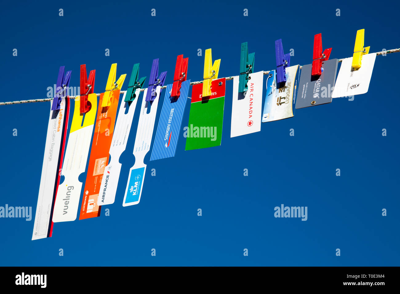 Hand luggage tags of different airlines hanging from a clothespin over a blue sky Stock Photo
