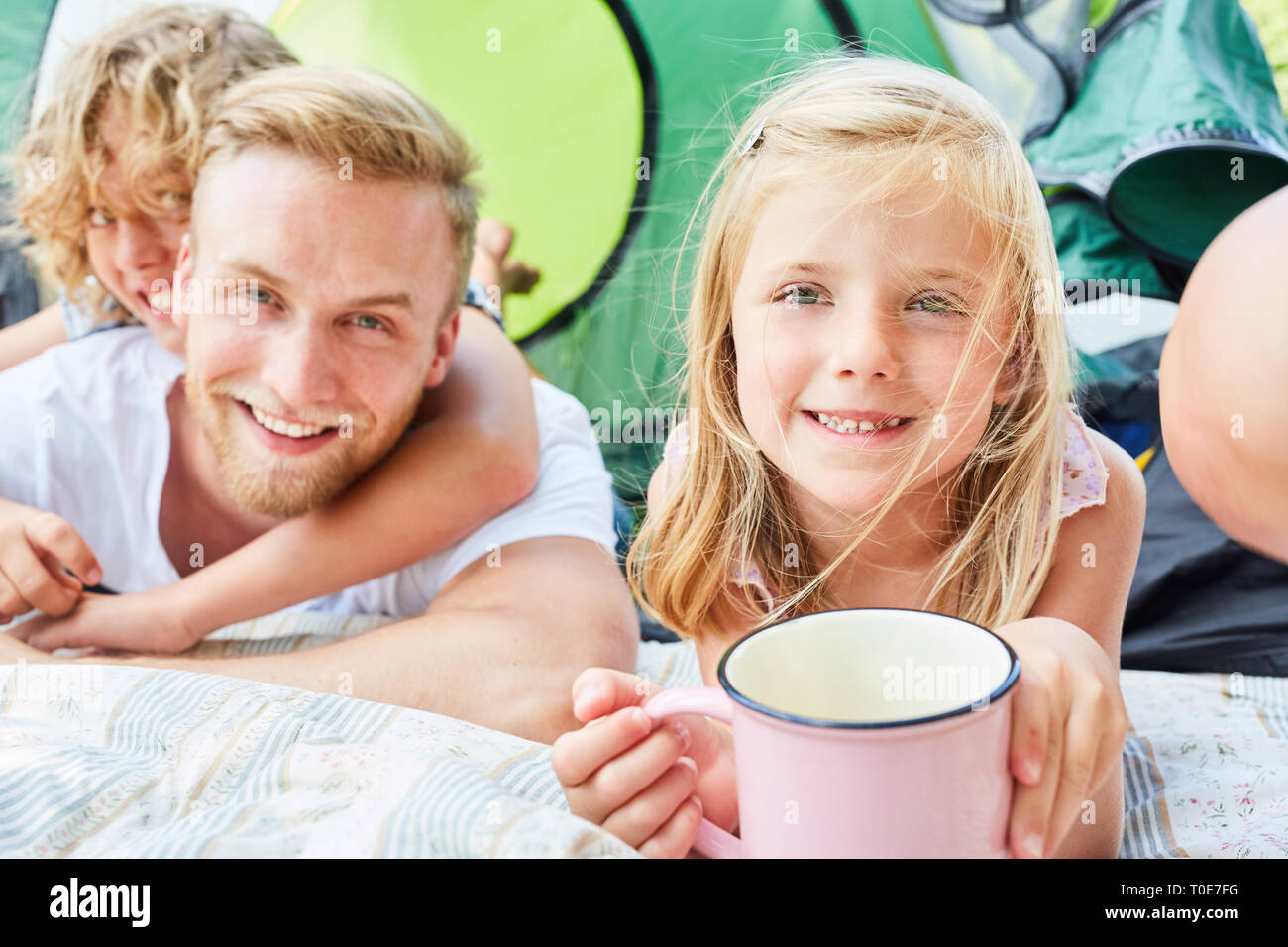 Father and two children on camping holiday in front of the tent together at breakfast Stock Photo