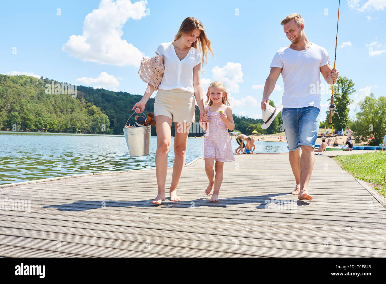 Happy family with daughter while walking on a footbridge at the lake in summer Stock Photo