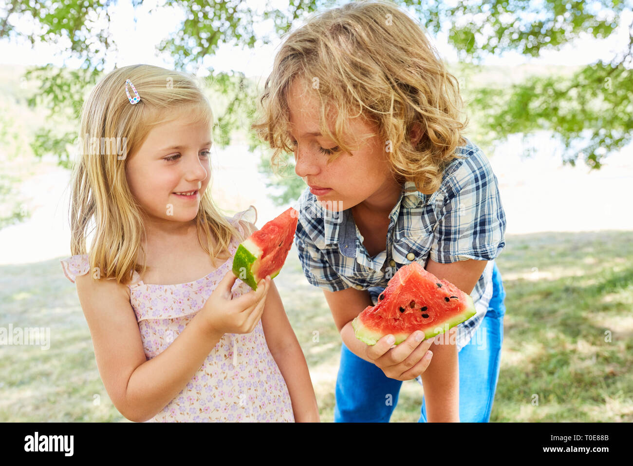 Little girl gives her brother a sweet piece of melon in the summer Stock Photo