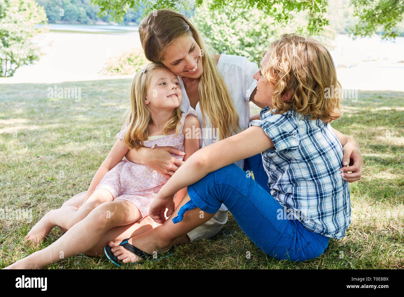 Mother and her two children are sitting relaxed together on a meadow in summer Stock Photo