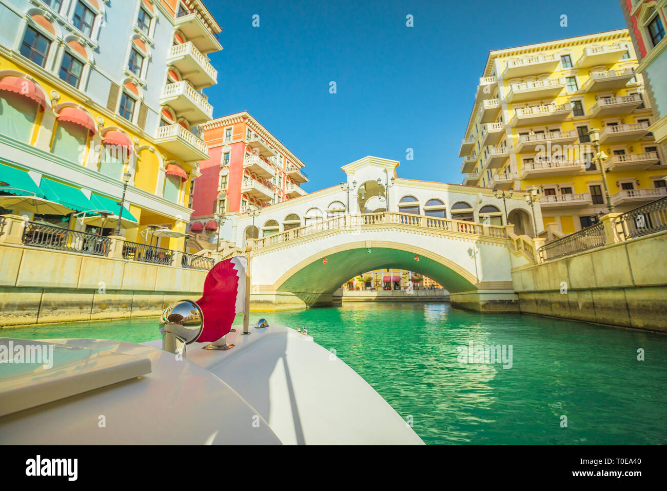 Venetian bridge on canals of picturesque Qanat Quartier icon of Doha, Qatar from a touristic boat with flag of Qatar. Venice at the Pearl, Persian Stock Photo