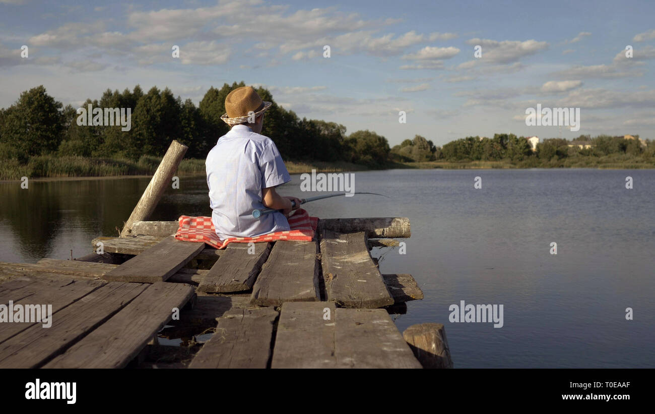 boy sits on the pier and catches fish Stock Photo