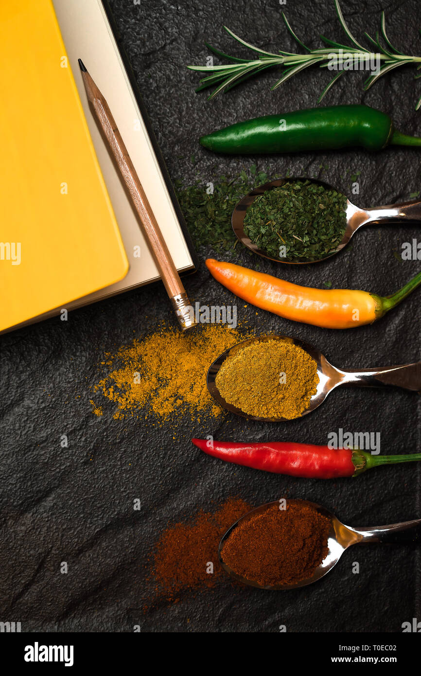 Top view on composition notebook for recipe and oriental spices in spoons and peppers on the black metallic tray in Asian style Stock Photo