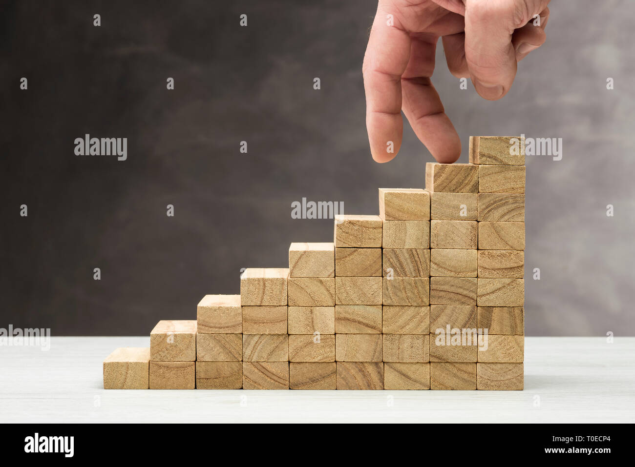 Concept of decrease. Graphic with wooden steps on grey background with hand coming down. Stock Photo