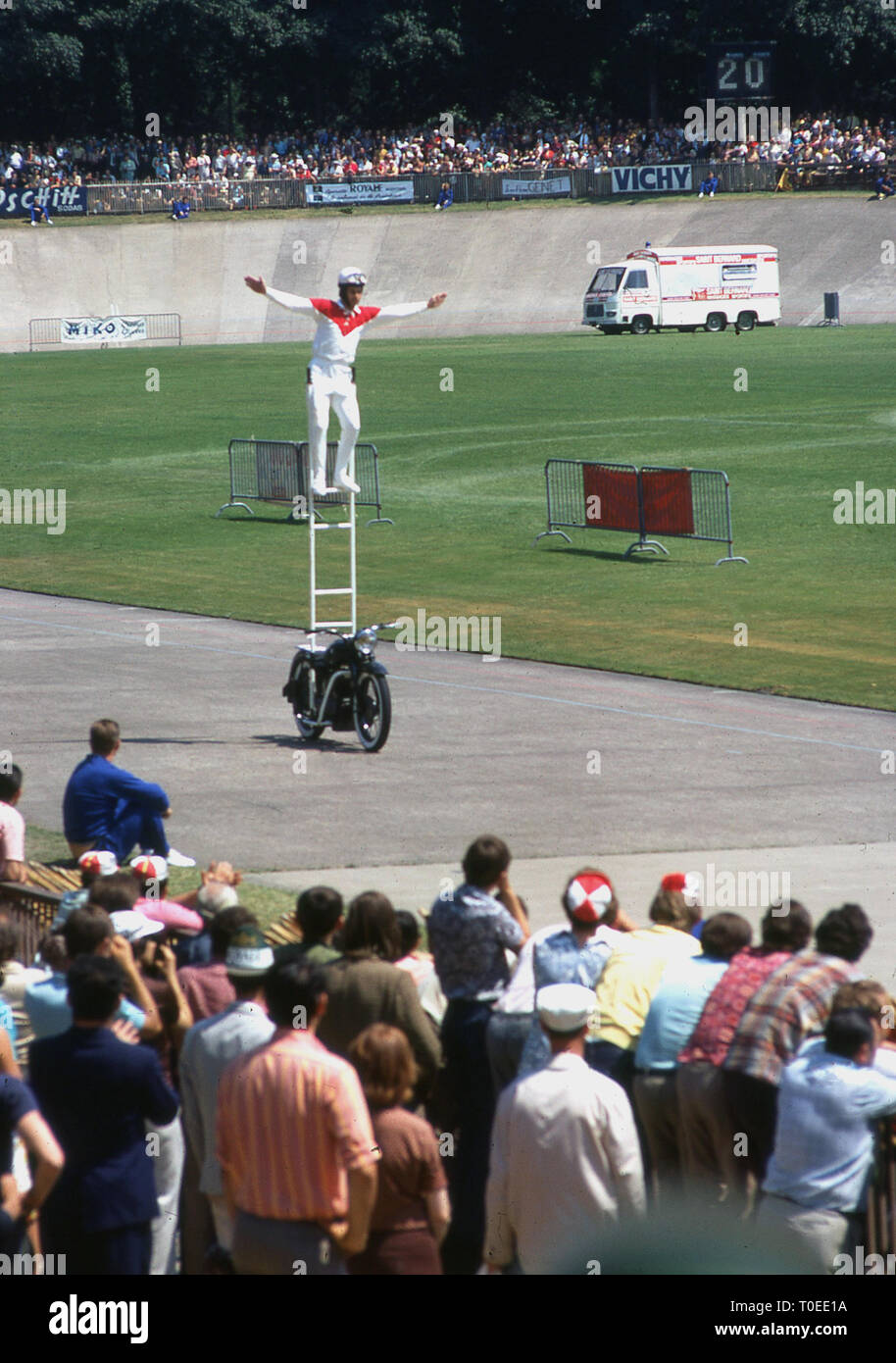 1974, tricks motorcyclist standing on a ladder riding a motorcycle entertaining the spectators at the finish of the Tour de France cycle race on the track at the Velodrome de Vincennes, Paris, France. This was the last year the Tour finished at the velodrome as the following year it moved to the Champs-Elysees. Stock Photo