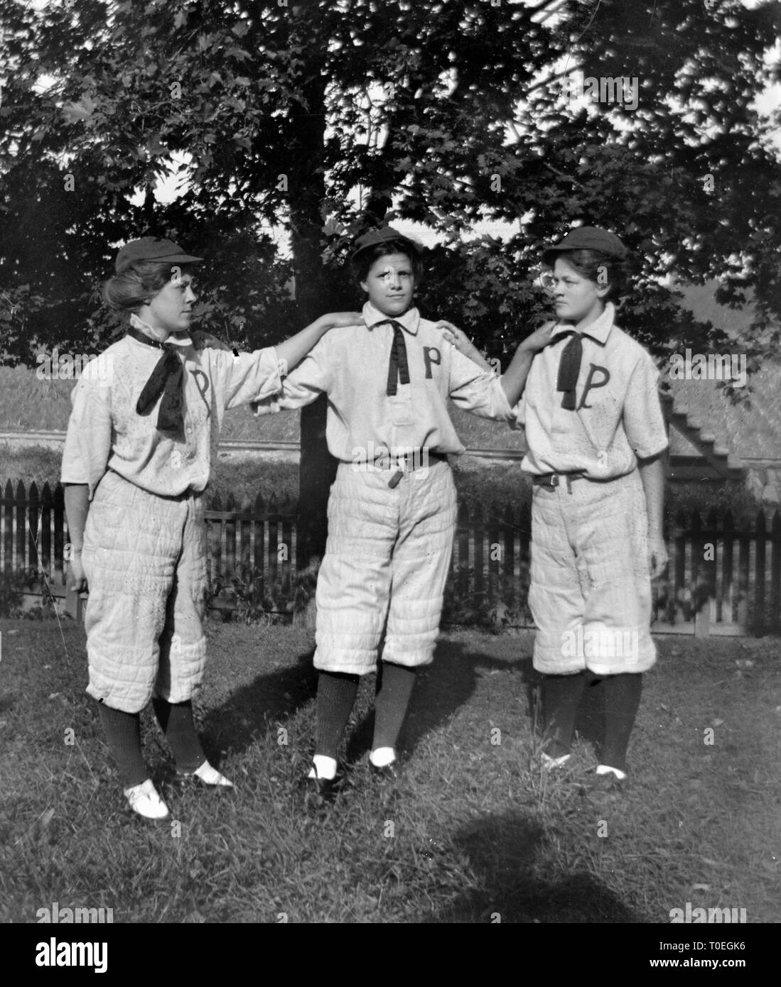 Three young women in baseball uniforms pose together in the backyard before the big game, ca. 1896. Stock Photo