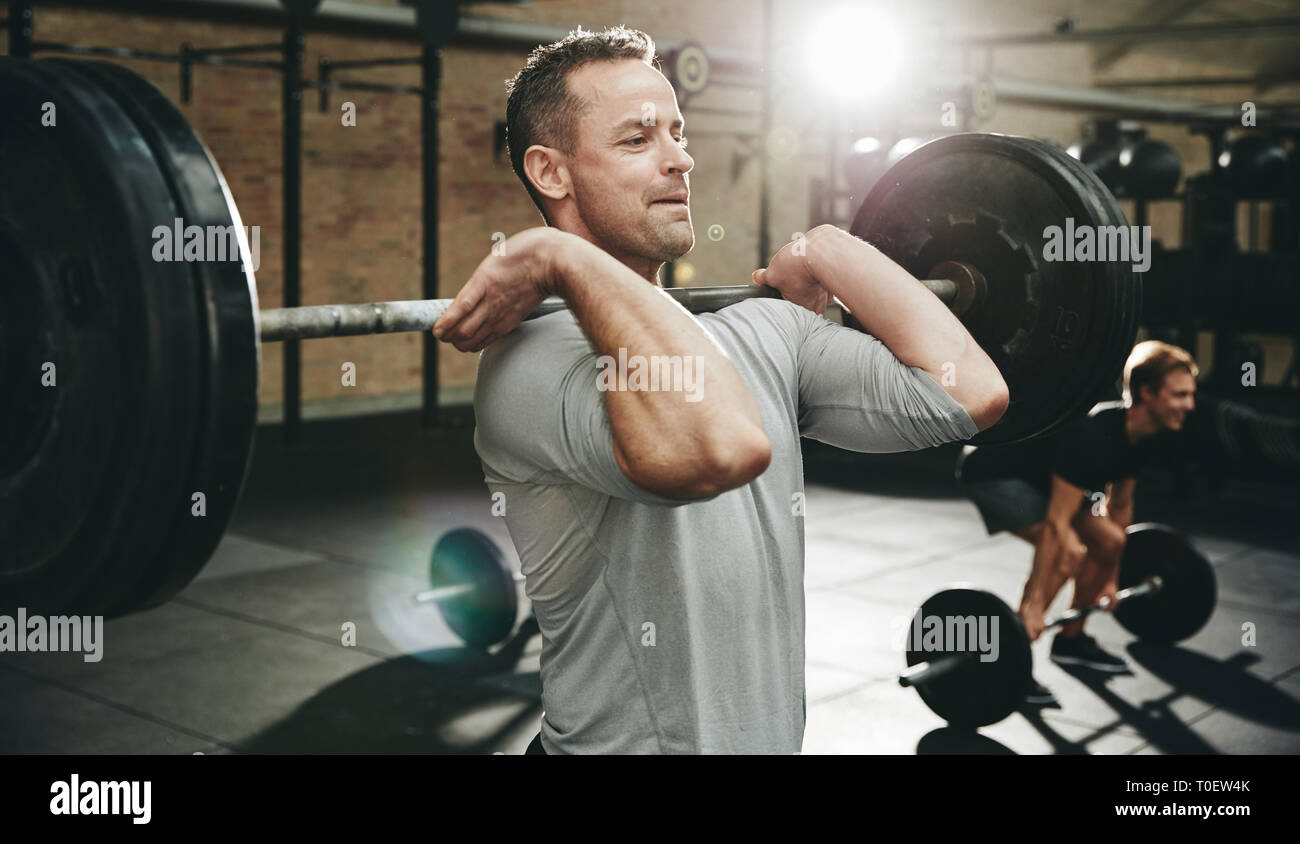 Fit man in sportswear focused on lifting weights during a strength training session at the gym Stock Photo