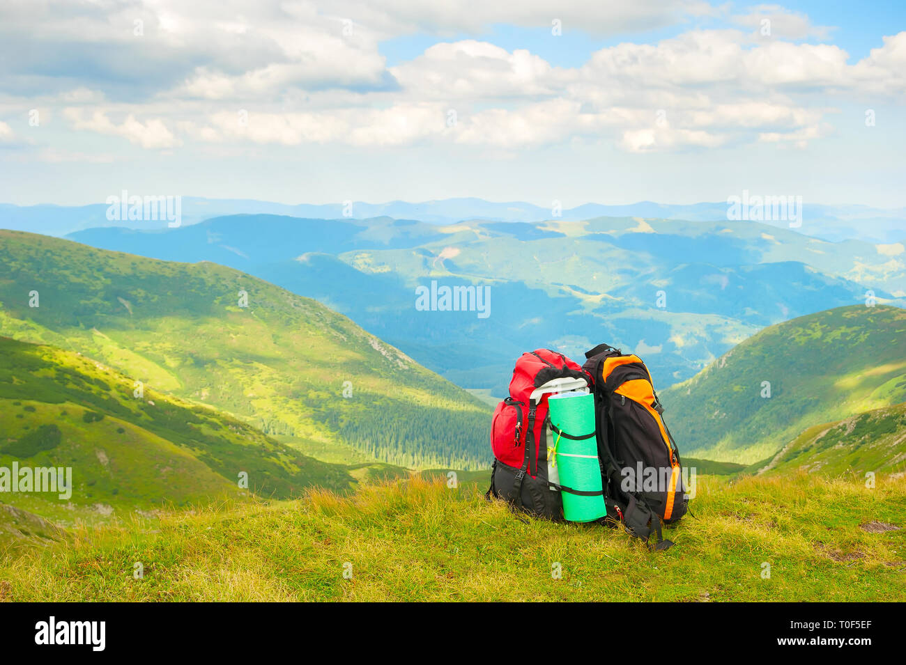 Two colorful hikers backpacks on green slope, scenic Carpathian mountains landscape in background, Ukraine Stock Photo