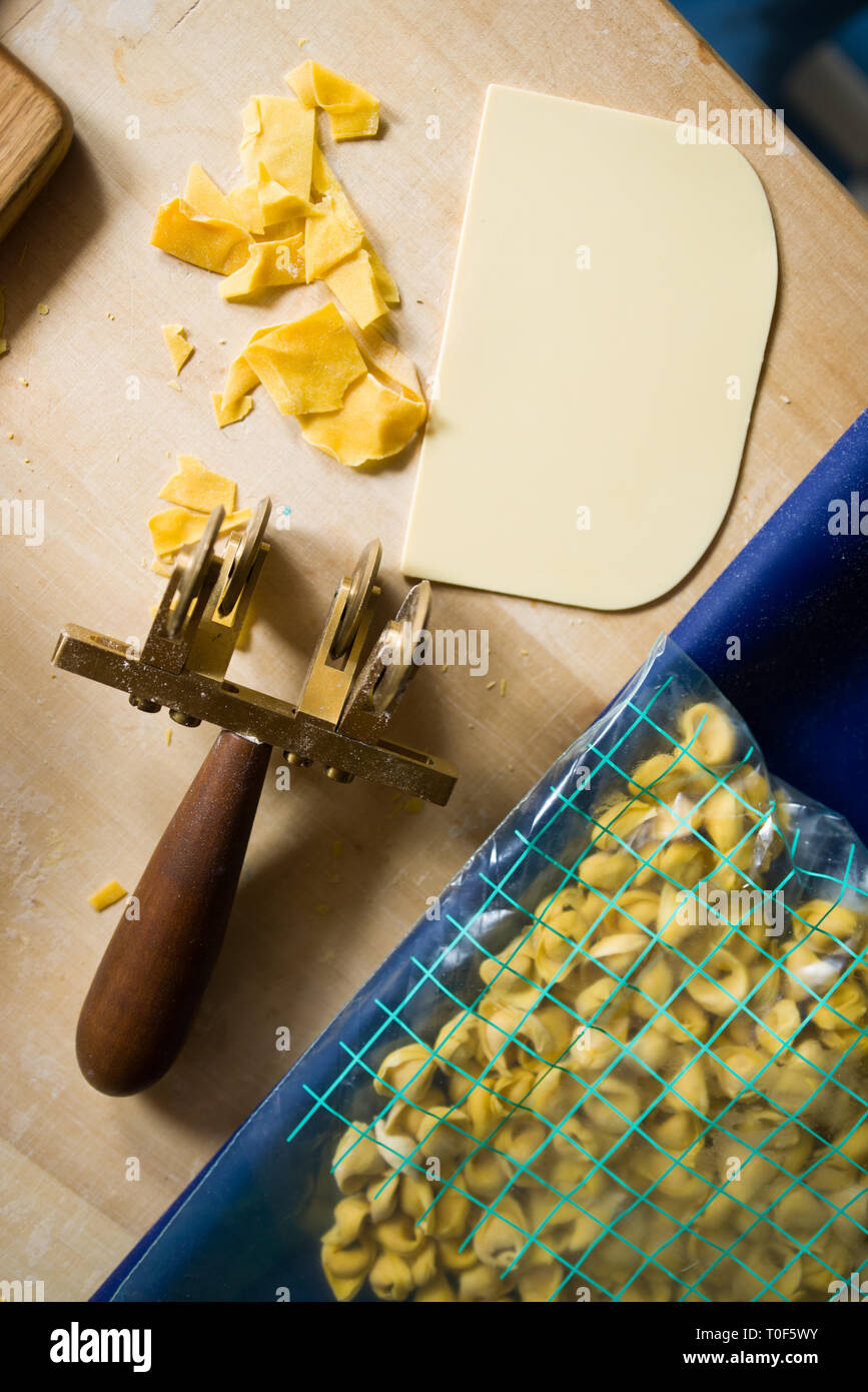 Dough cutter wheel, a marysa plastic spatula to cut  dough and a plastic bag with tortellini ready made , over a wooden background Stock Photo