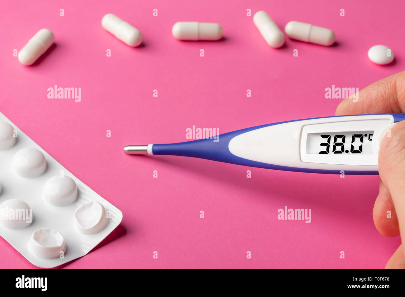 Electronic thermometer and pills on a pink background. High temperature