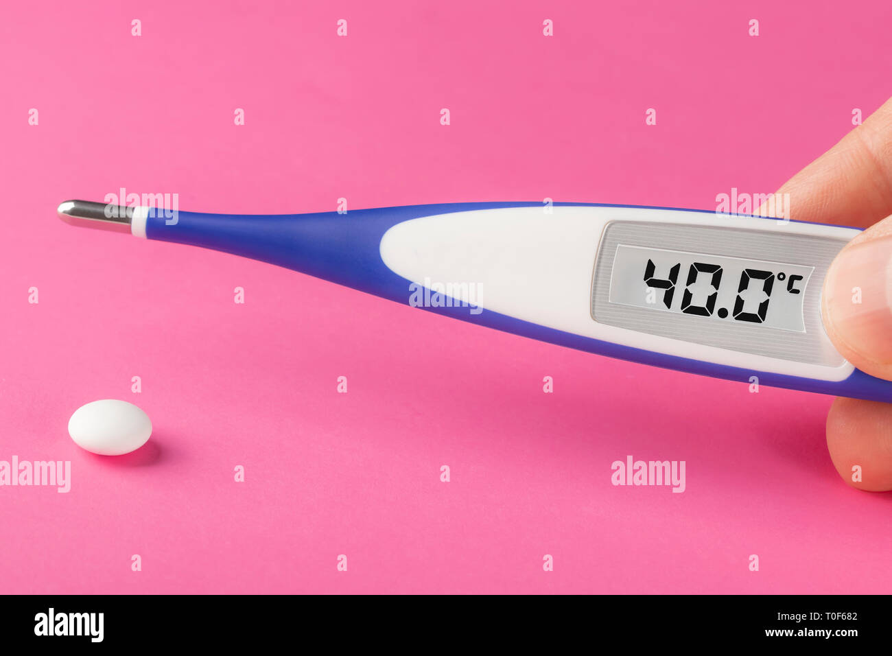 Electronic thermometer and pill on a pink background. High temperature 40 degrees Celsius on display. Copy space. Stock Photo