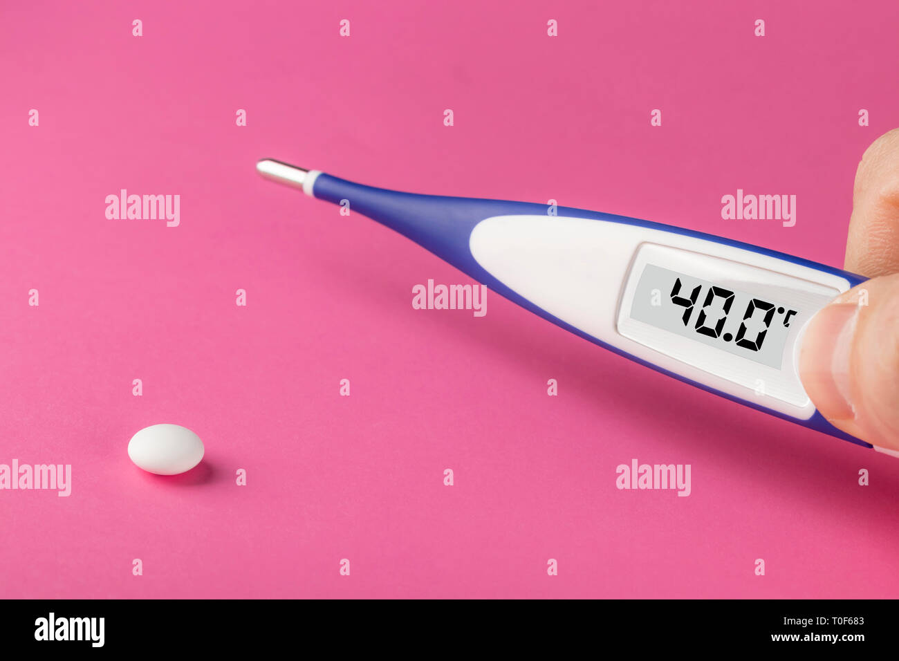 Electronic thermometer and pill on a pink background. High temperature 40 degrees Celsius on display. Copy space. Stock Photo
