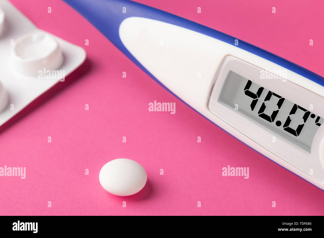 Electronic thermometer and pills on a pink background. High temperature 40 degrees Celsius on display. Copy space. Stock Photo