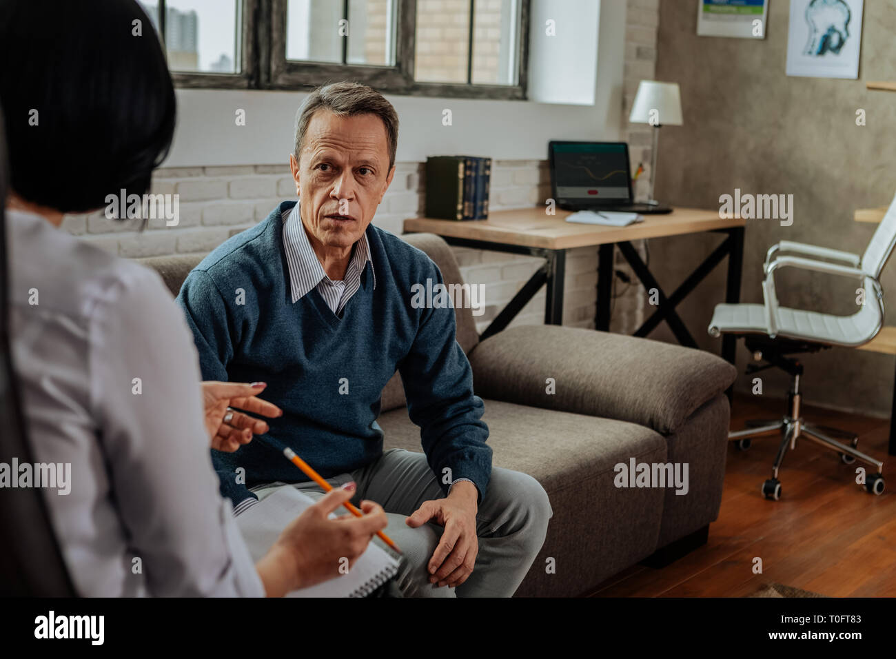 Disturbed adult guy in blue cardigan being shocked during conversion with doctor Stock Photo