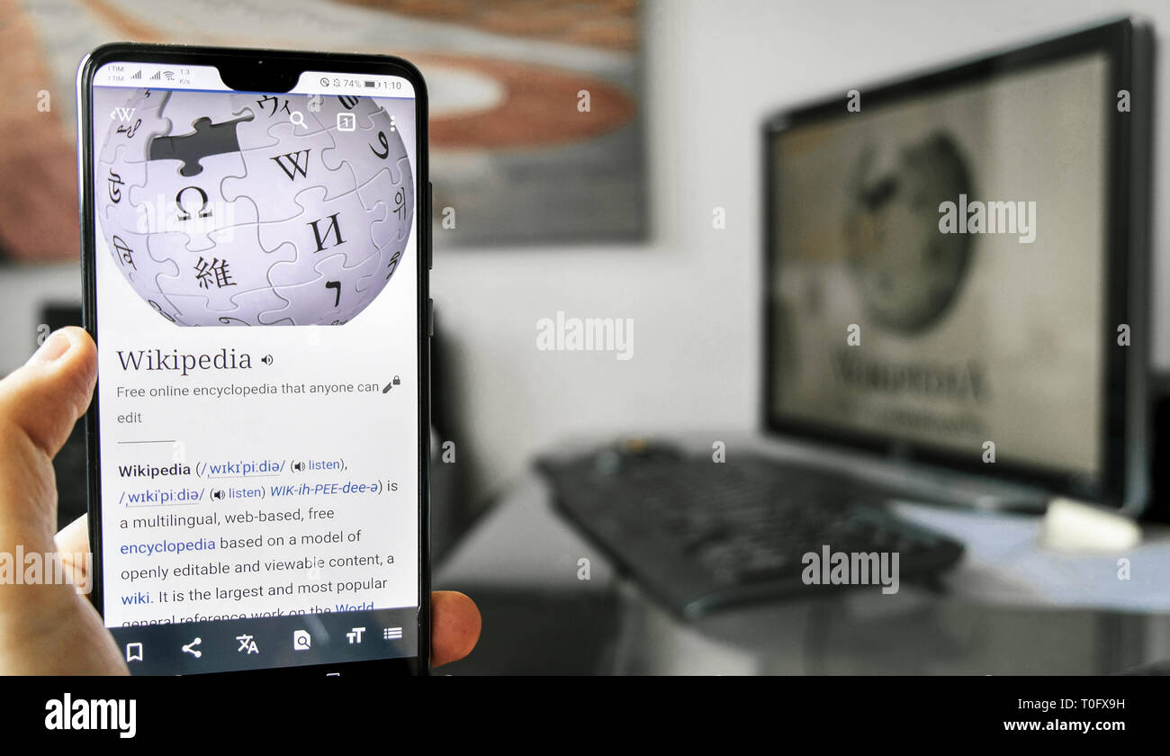 Wikipedia app smartphone computer desk background Stock Photo