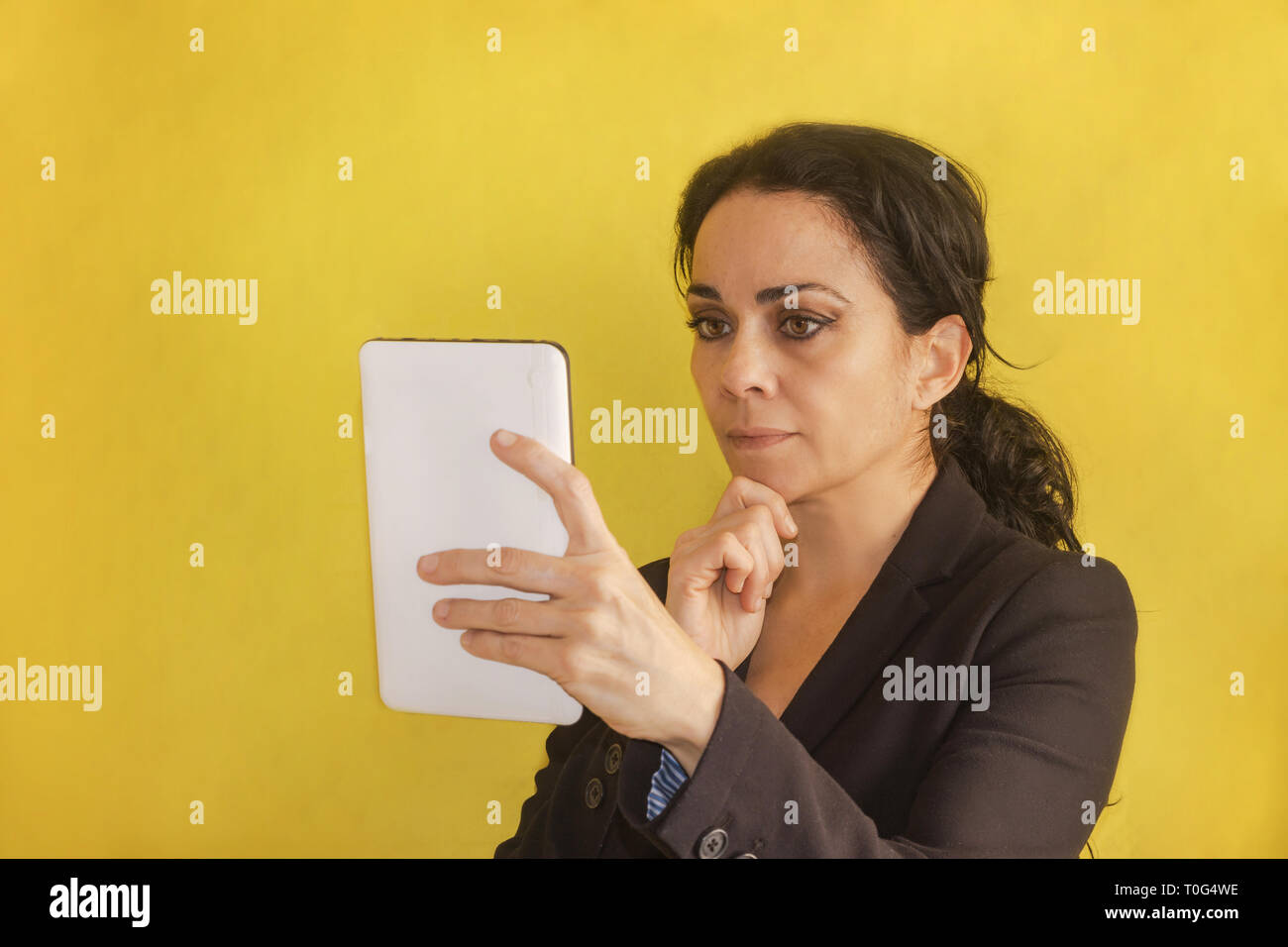 Beautiful young business woman, with pigtail, black jacket, isolated on a background, looking at her tablet. Woman analyzing data Stock Photo