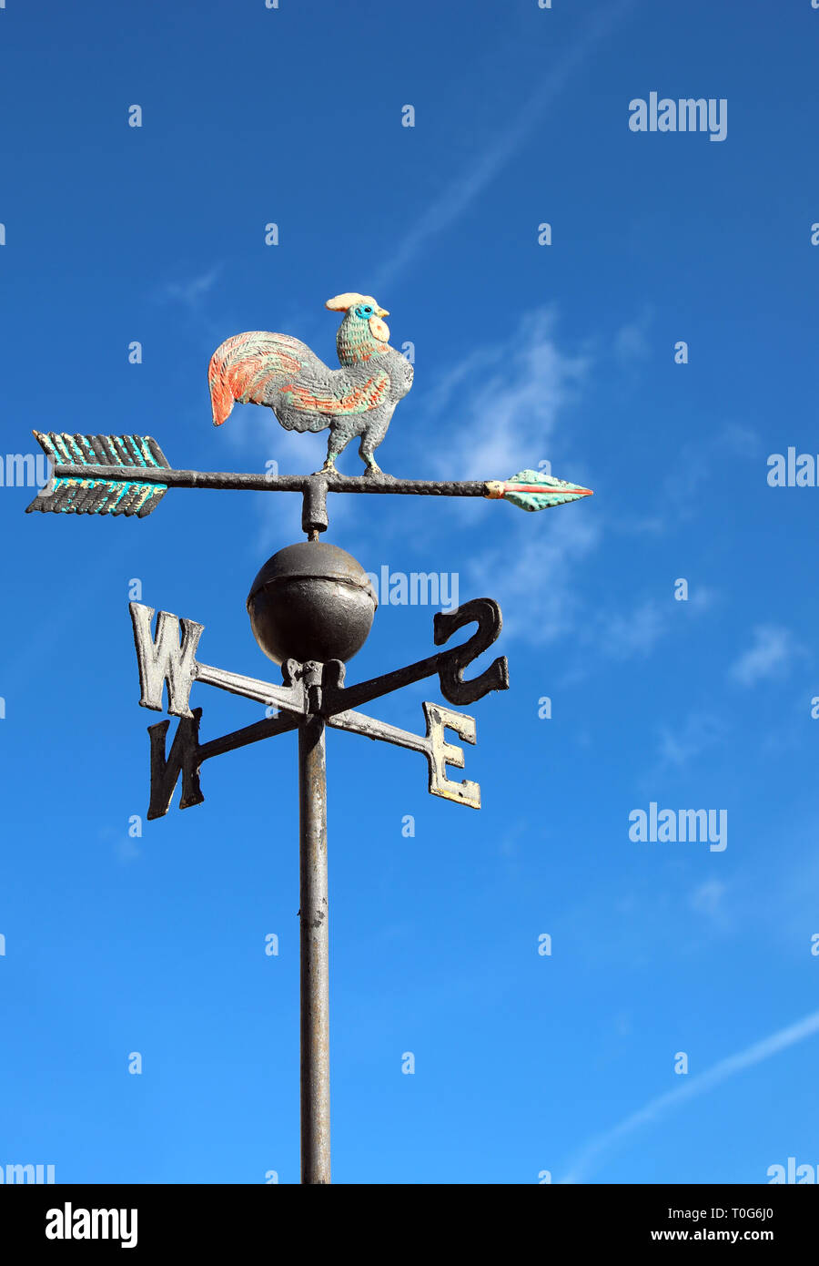 old wind vane with cock on top and cardinal points on the blue sky
