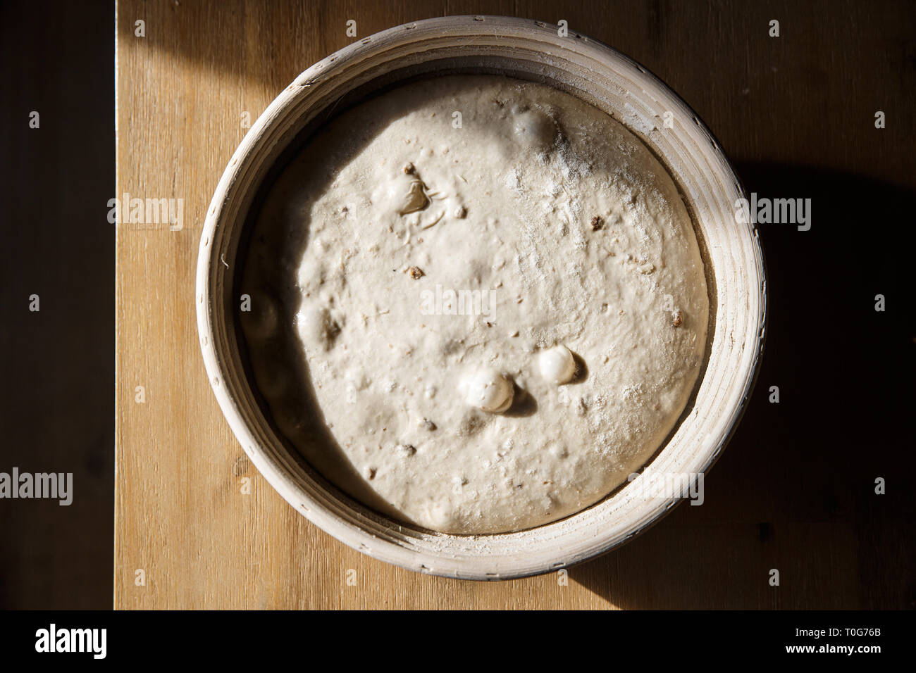 Sourdough bread proofing in a basket with visible gas bubbles. Homemade
