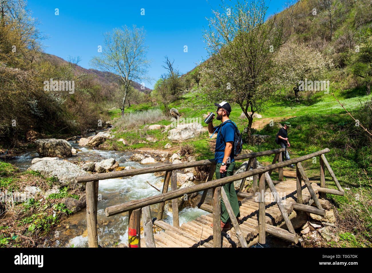 Man drinking water the wooden bridge over small river outdoors Stock Photo