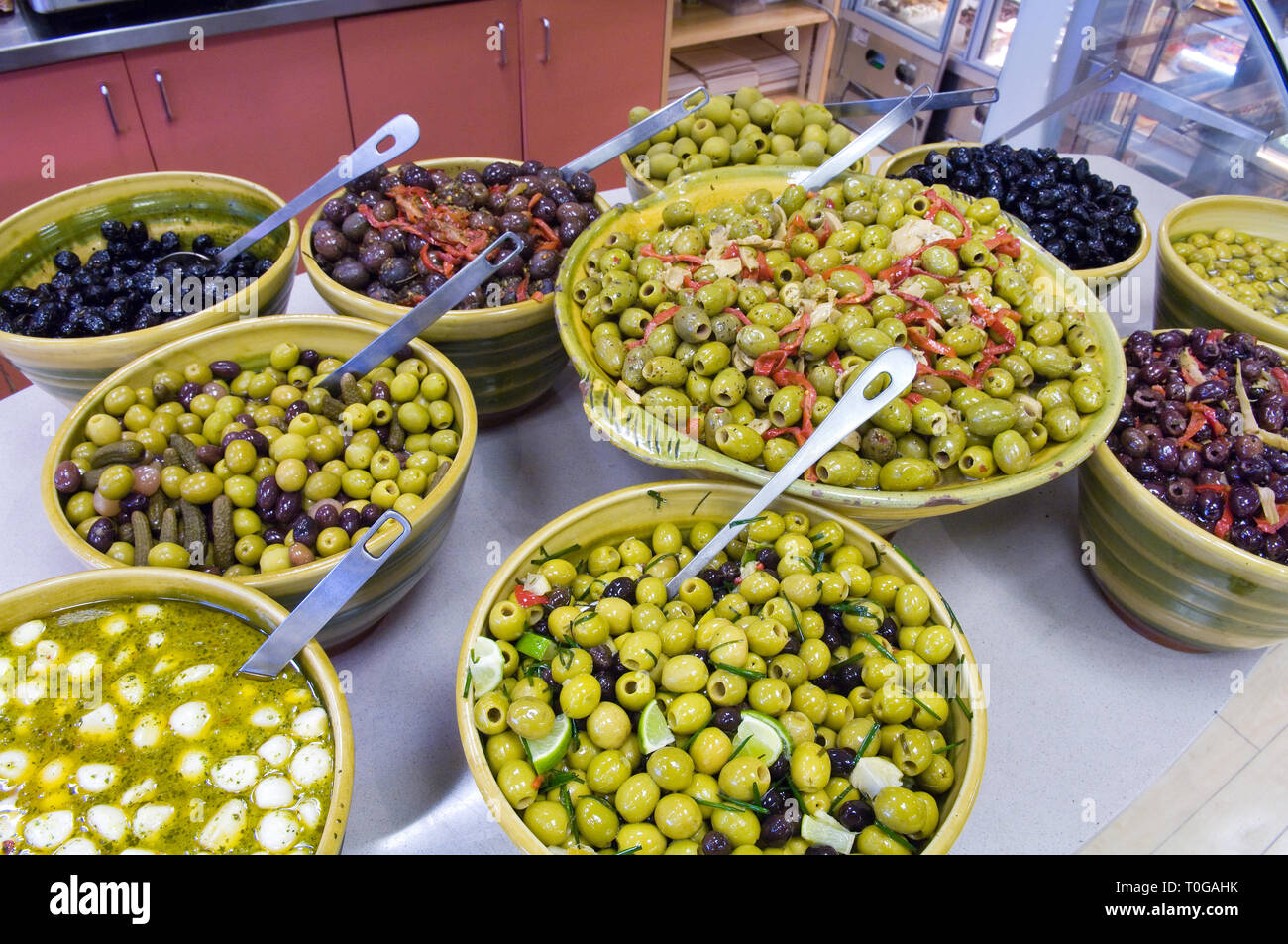Lots of different types of olives for sale by weigh and displayed in large bowls for sale in a deli. Stock Photo