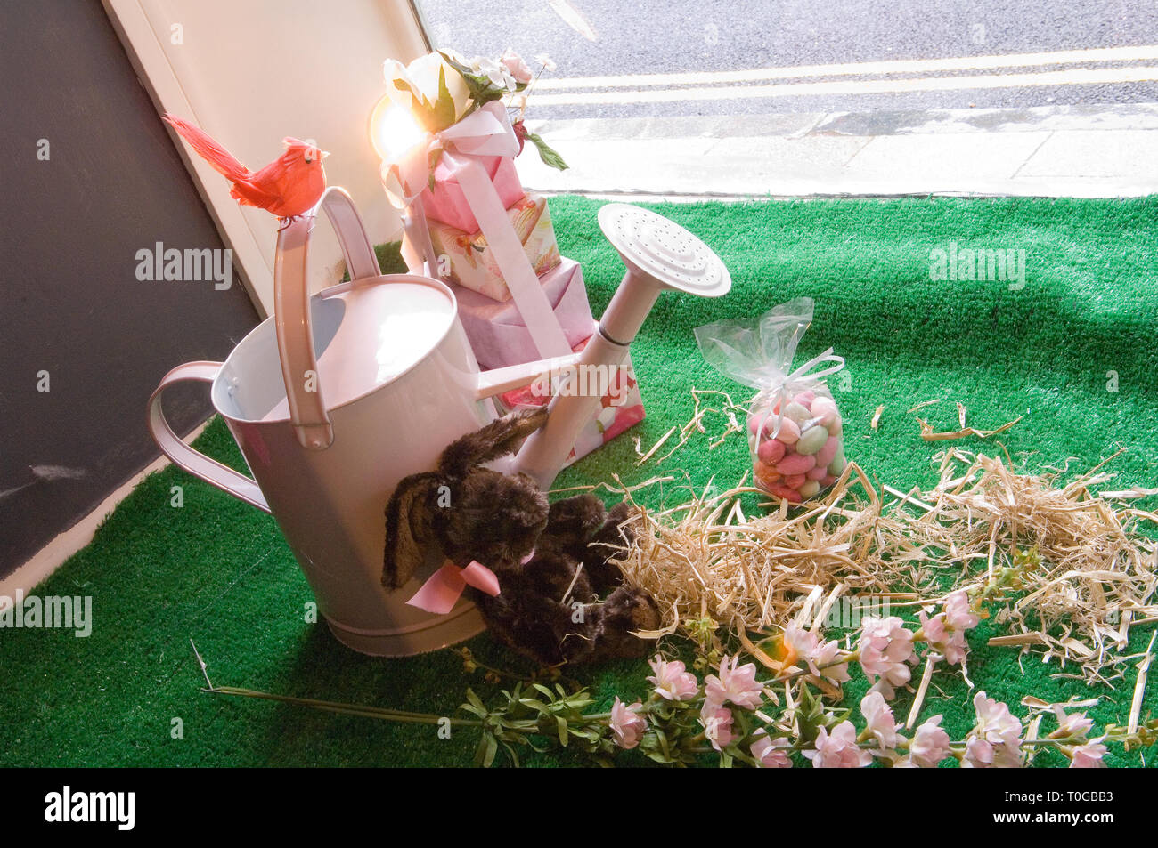 A pink watering can on display as part of a fun shop window display with an Easter theme Stock Photo