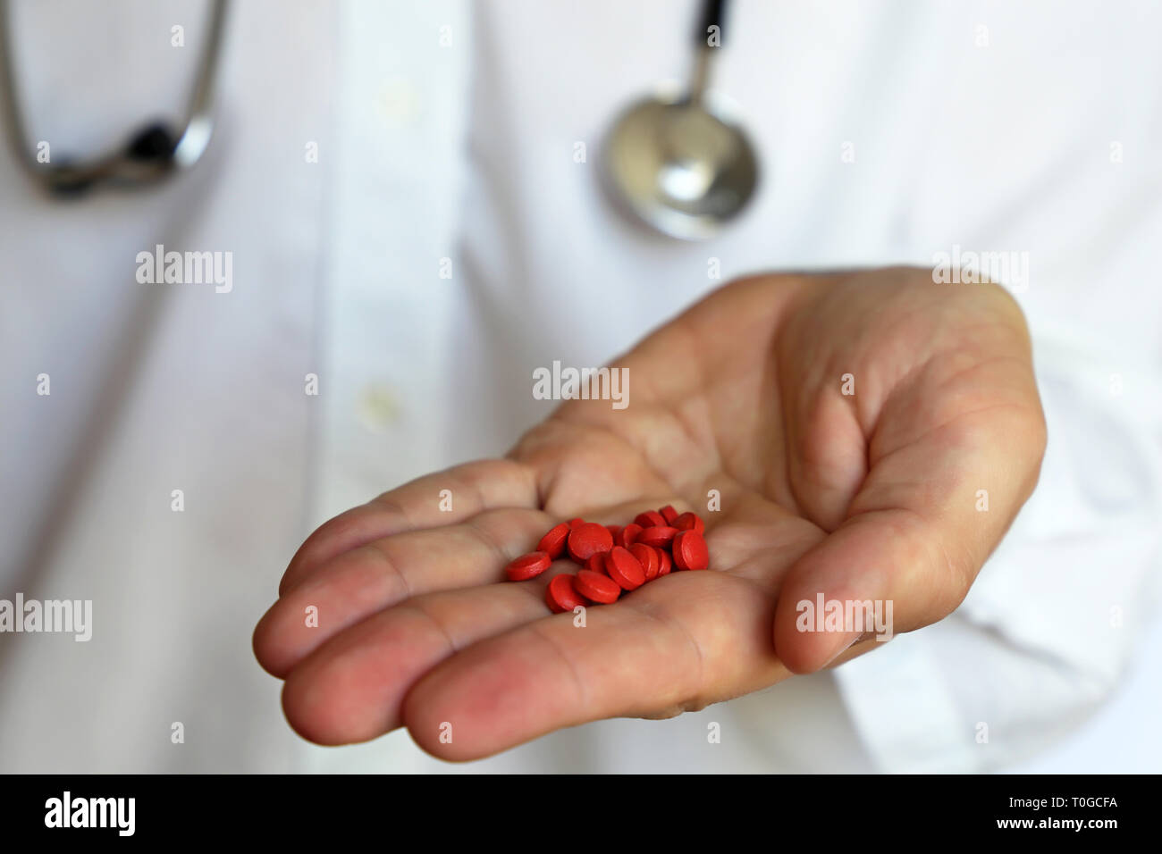 Therapist at the clinic, doctor with red pills, man with stethoscope giving medication in capsules. Concept of medical prescription, dose of drugs Stock Photo