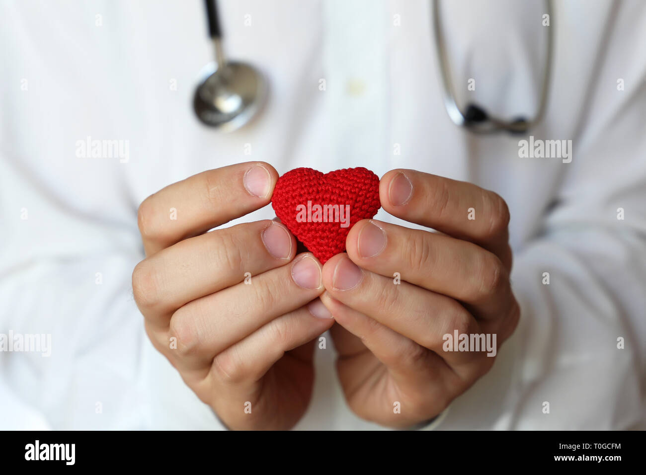 Cardiology and health care, doctor holding red knitted heart in hands. Concept of cardiologist, blood donation, treatment of heart disease in clinic Stock Photo