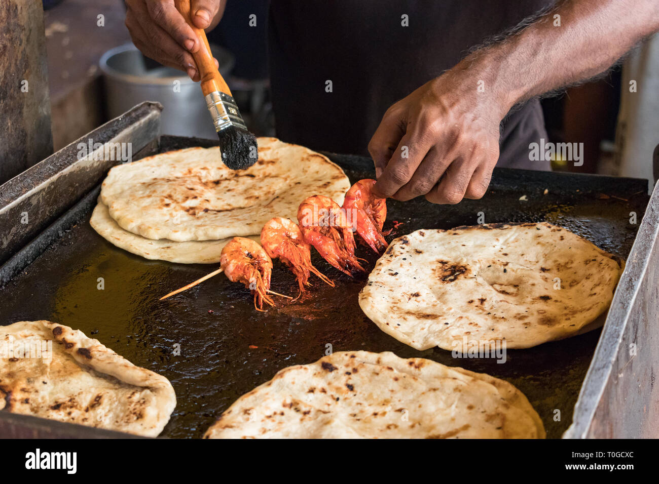 Male hand of a cook, cooking prawns with pol roti flat bread tn the ...