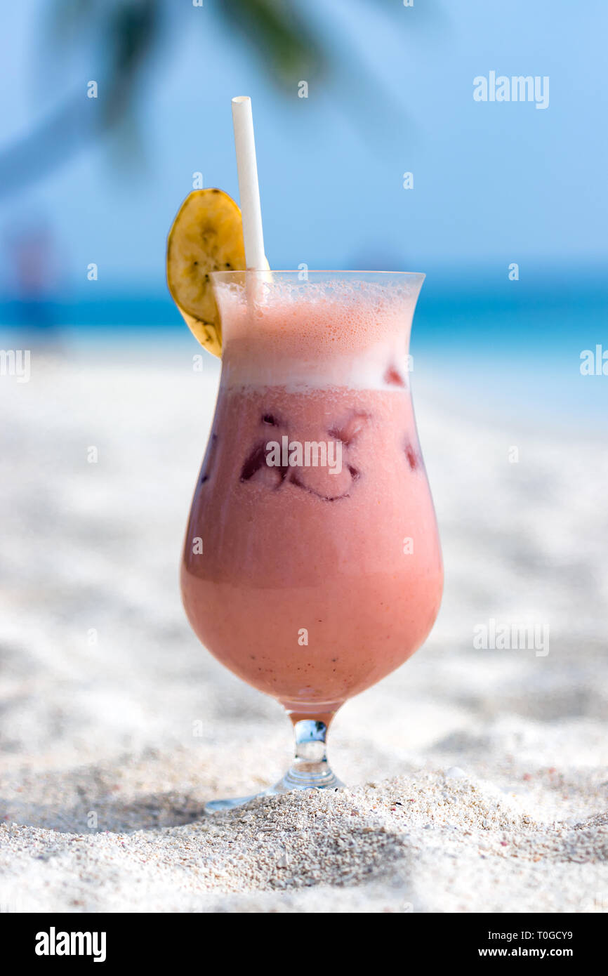 Cocktail with fruits, a slice of banana on the top and straw on the sand at a beach in Maldives. Stock Photo