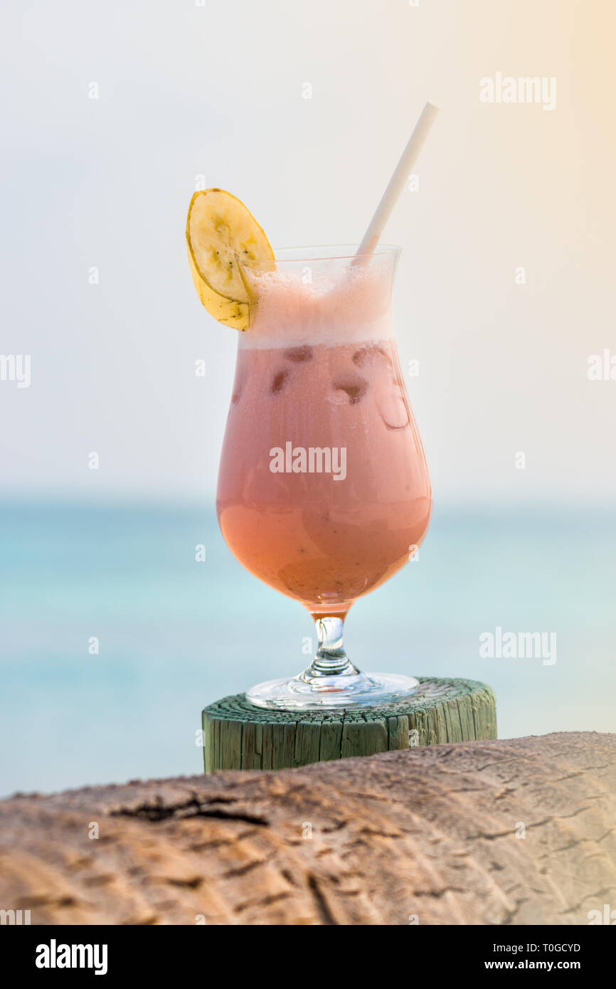 Cocktail with fruits, a slice of banana on the top and straw on a piece of wood in Maldives. Stock Photo