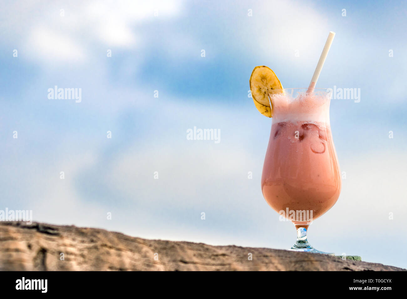 Cocktail with fruits, a slice of banana on the top and straw on a piece of wood in Maldives. Stock Photo