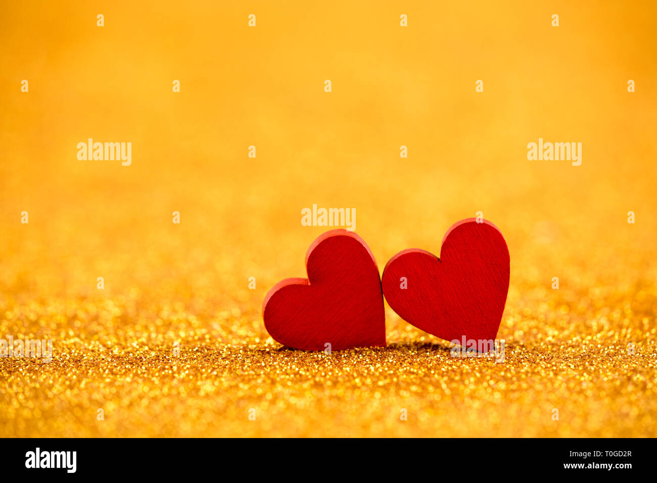 Two red hearts on golden glitter background in love concept Stock Photo