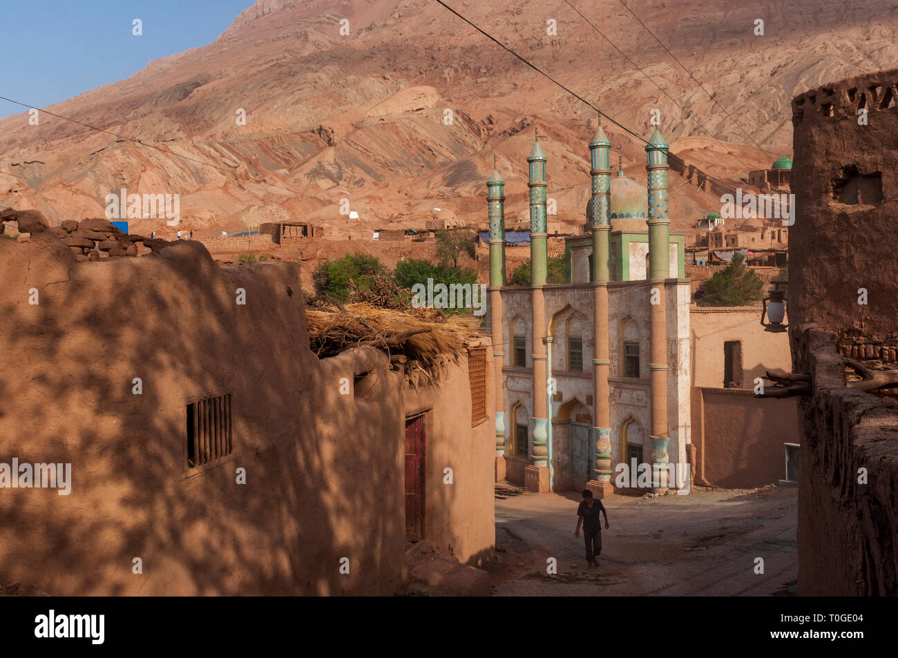 Tuyog, Turpan, China - August 12, 2012: A man passing in front of the mosque at the Uyghur village of Tuyog, with mountains on the background, Xinjian Stock Photo