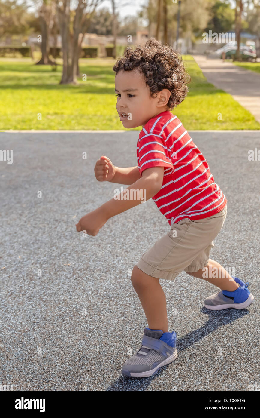 The little boy starts to run. He sees some kids at the park and makes run towards them. Stock Photo