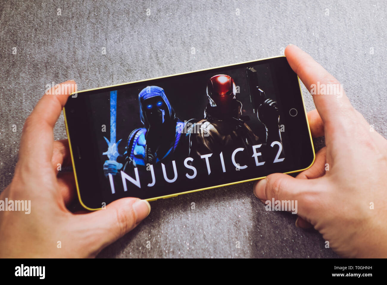 Berdyansk, Ukraine - March 4, 2019: Hands holding a smartphone with Injustice 2 game on display screen. Stock Photo