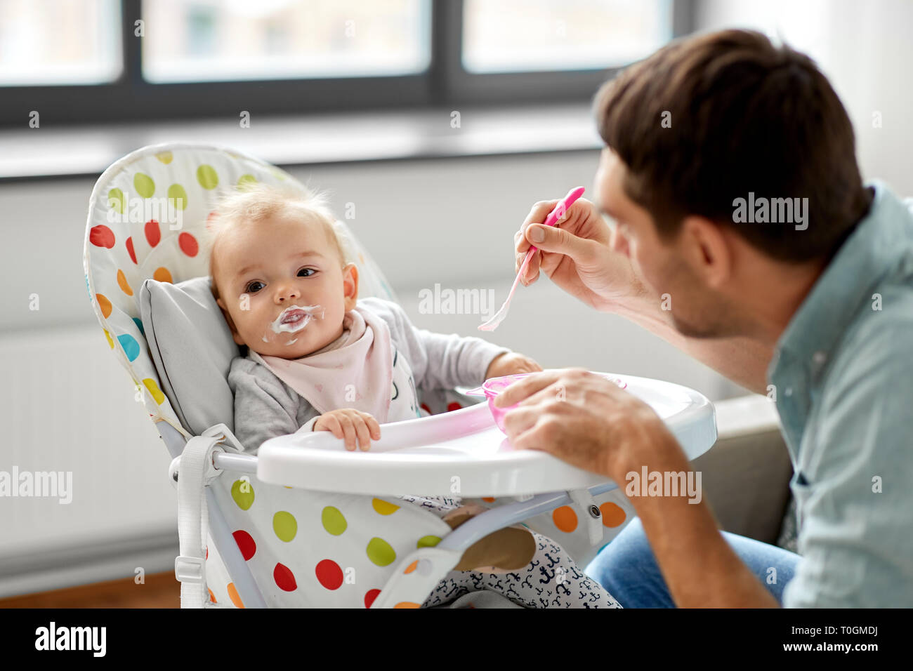 father feeding baby in highchair at home Stock Photo