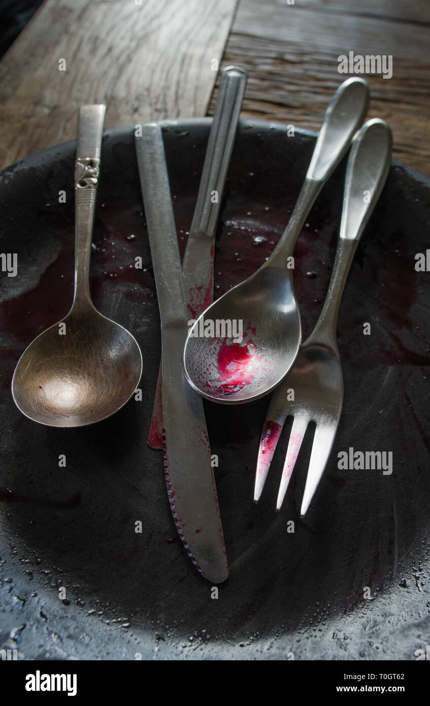 dirty silverware on a dirty plate covered with blueberry sauce after a meal Stock Photo