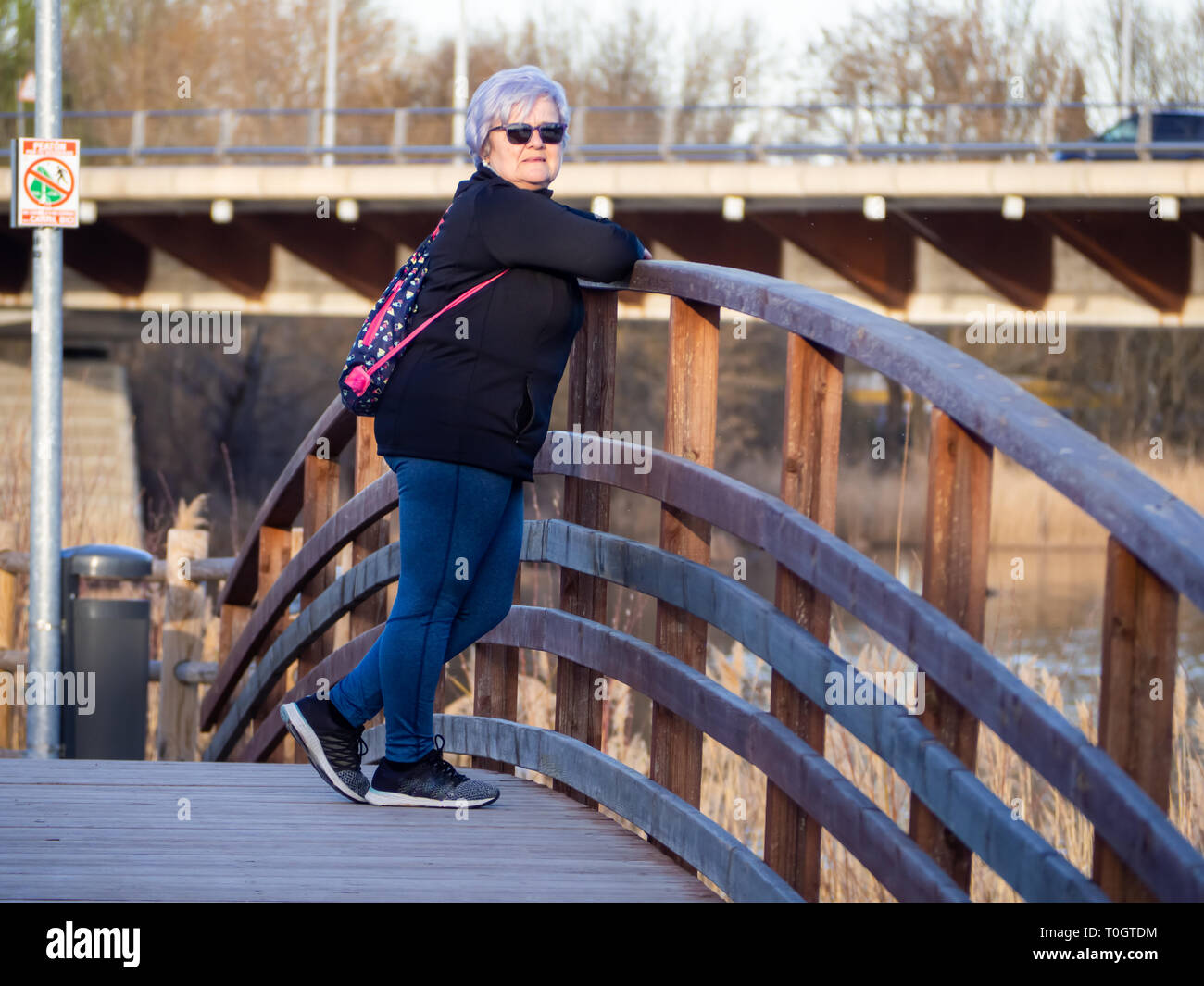 A senior woman with white hair posing in a wooden bridge Stock Photo