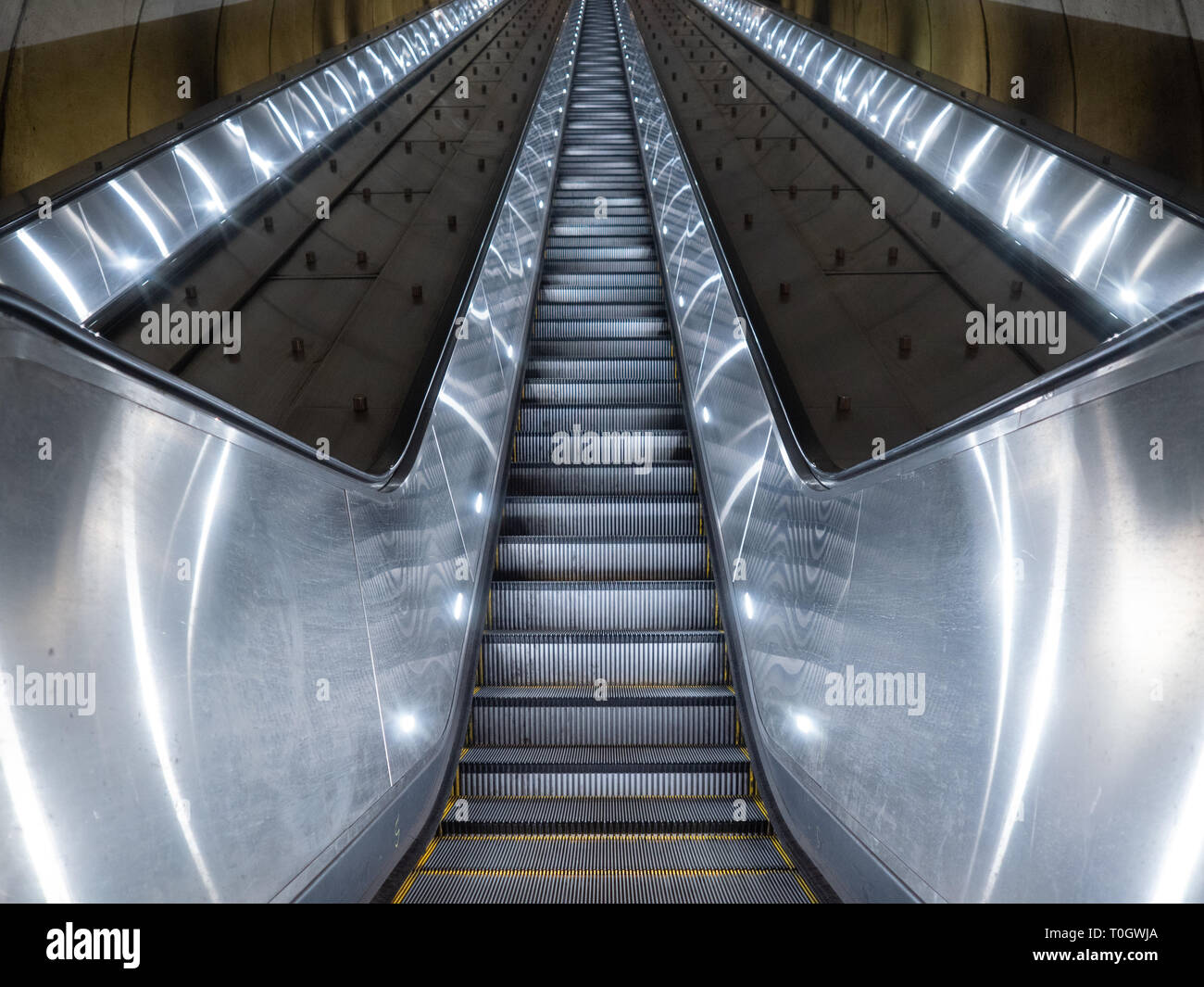 Washington DC, United States - 3 March 2019. Long escalator leading up from Adams Morgan Metro station through concrete tunnel illuminated in cold, me Stock Photo
