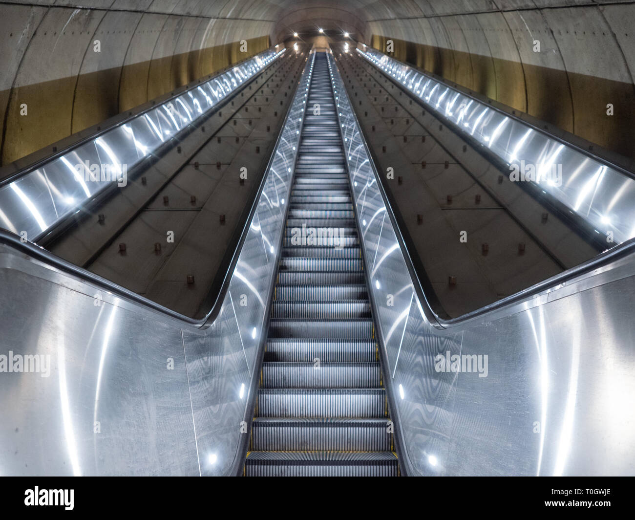 Washington DC, United States - 3 March 2019. Long escalator leading up from Adams Morgan Metro station through concrete tunnel illuminated in cold, me Stock Photo