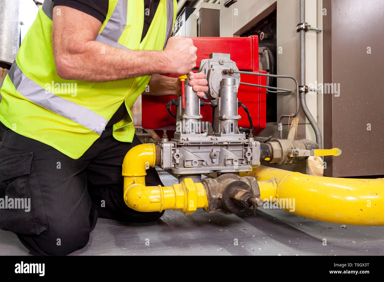 Gas engineer in yellow high visibility vest fitting a valve to an