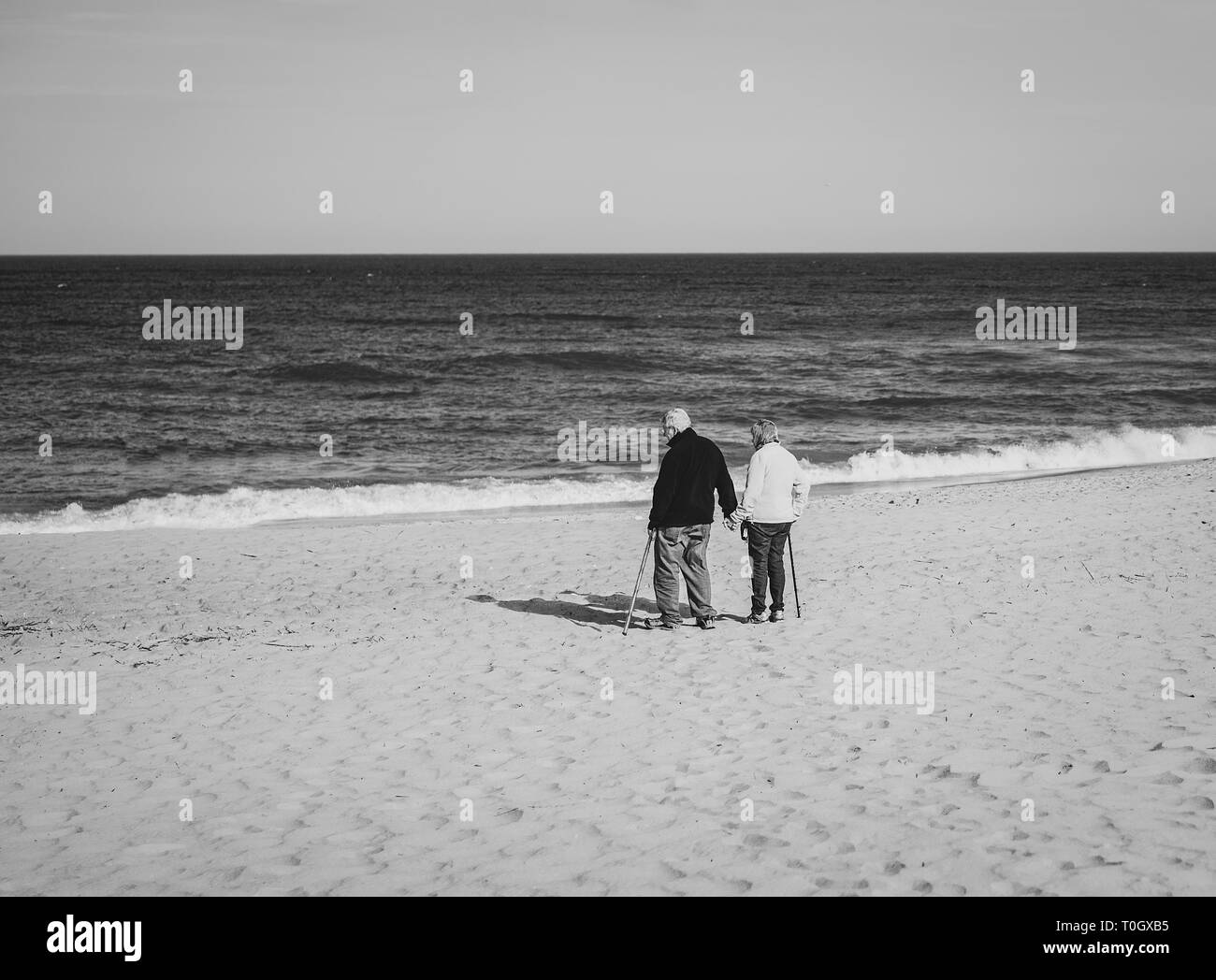 An old couple walk onto the beach with their canes, holding hands Stock