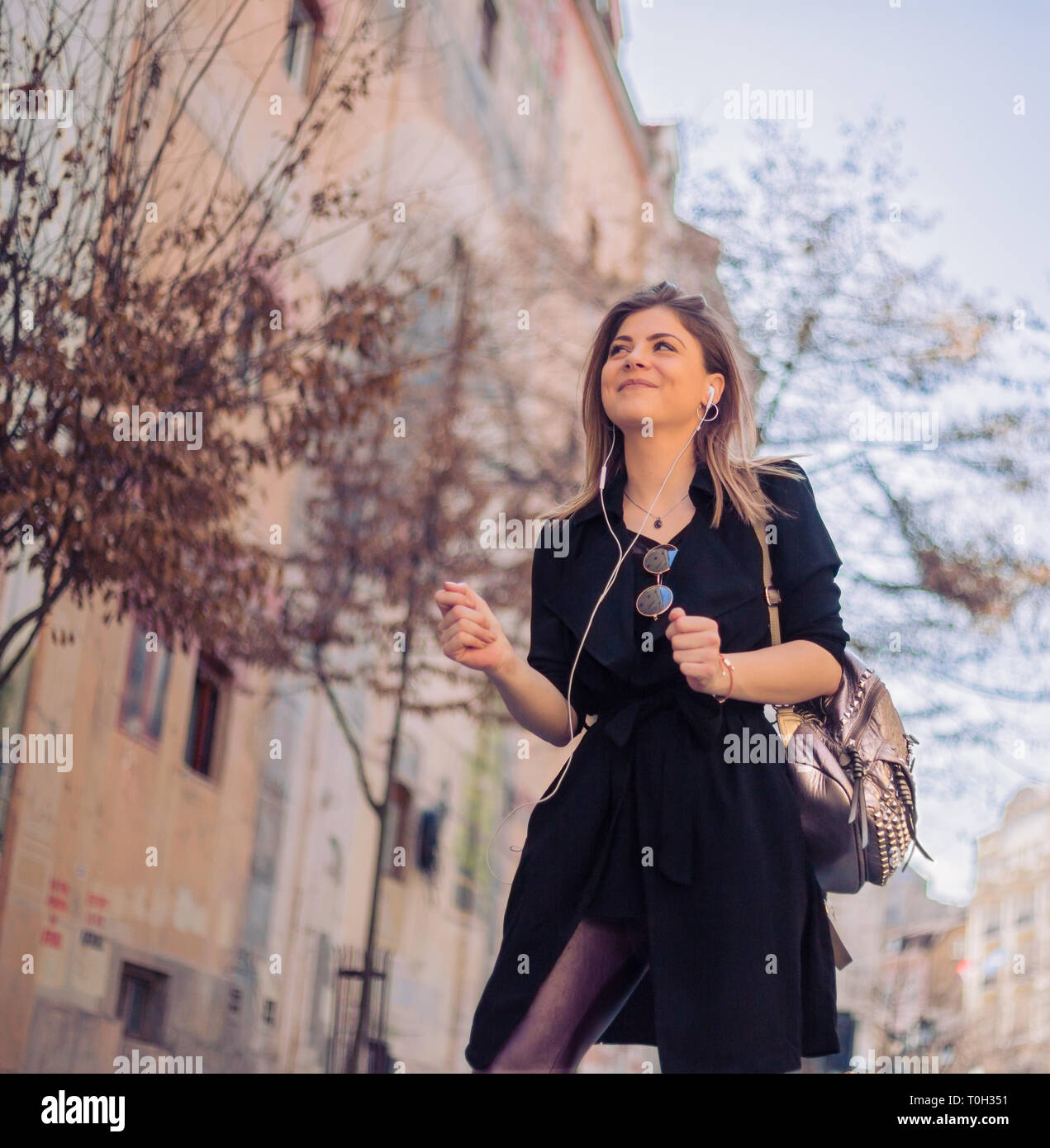 Young, beautiful and fashionable woman walking on the vintage street with headphones and enjoying the music Stock Photo