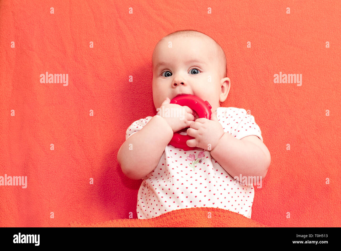 Head and shoulders portrait of little baby girl chewing teething ring